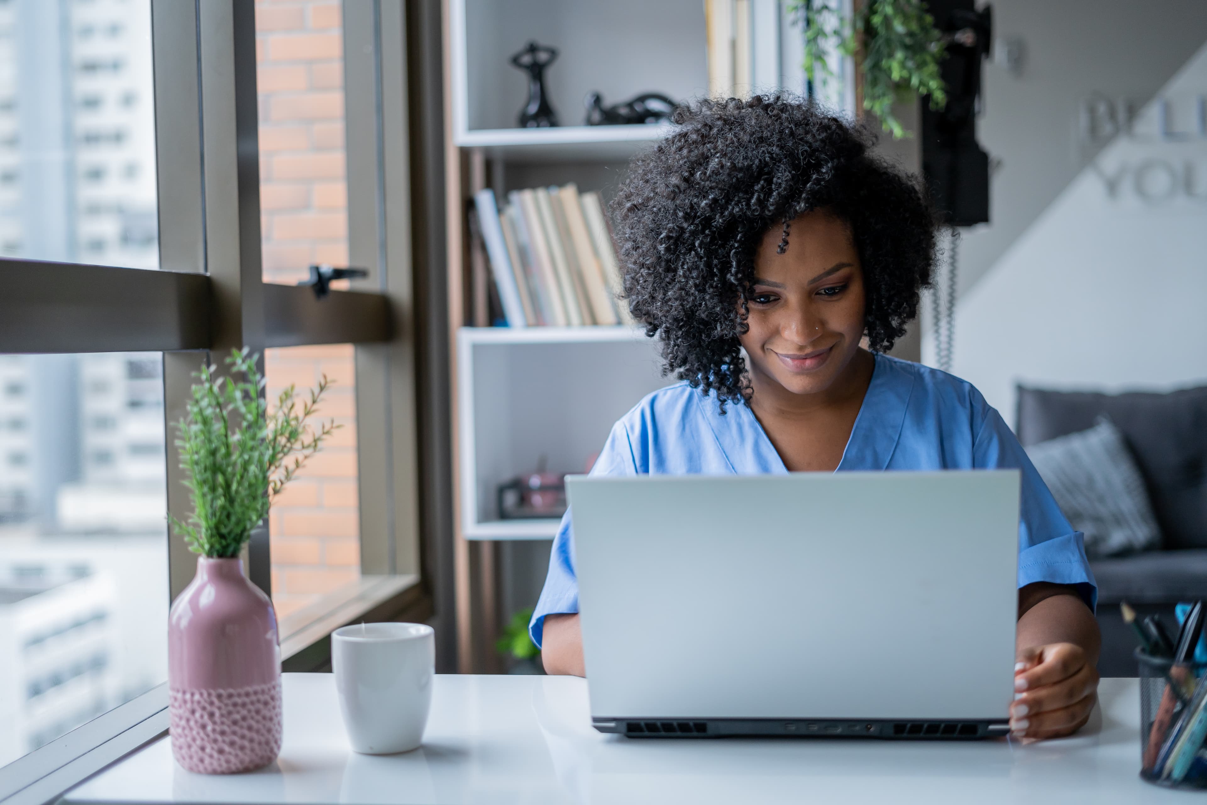 woman nurse on her computer at desk next to window healthcare sourcing nursing talent iStock-1401542006