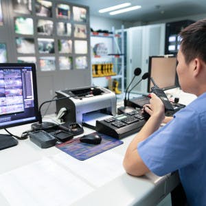 An image of a cleared candidate with a walkie-talkie at a security controls desk in the aerospace and defense industry