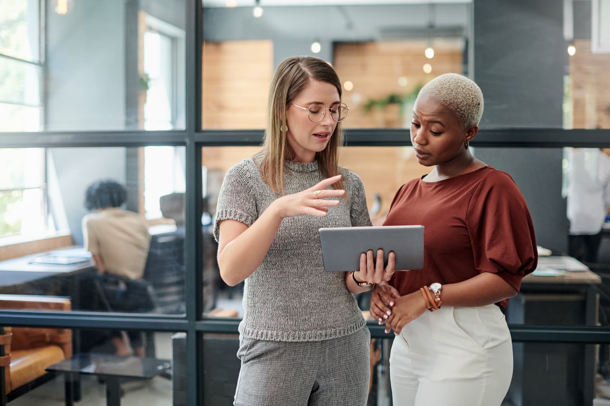Two women having a discussion while looking at a tablet.